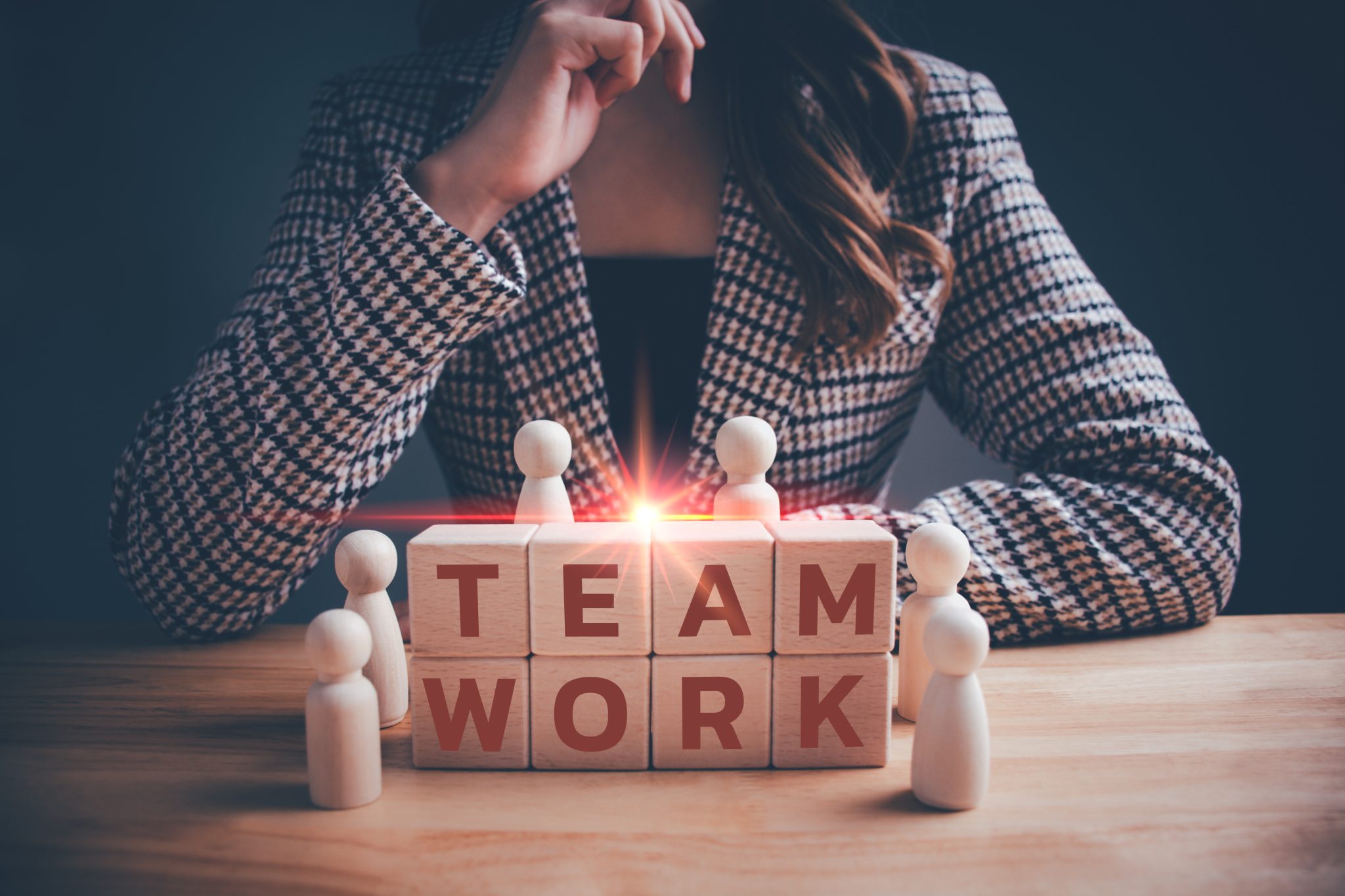 Das Bild zeigt Holzfiguren um die Buchstabenblöcke „TEAMWORK“ und symbolisiert Zusammenarbeit und Partnerschaft.